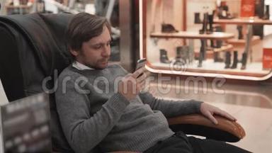 商场里的男人躺在<strong>按摩椅</strong>上，近距离拍摄，使用智能手机